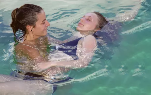 A practitioner holds a woman gently as she floats through the water with her eyes closed.