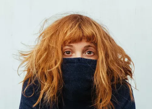 A woman with red hair with a jumper pulled up over her face. 