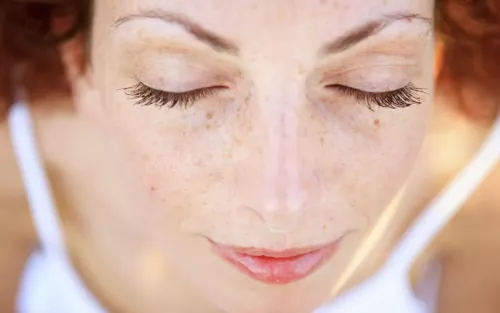 A woman with red hair and freckles with her eyes closed.