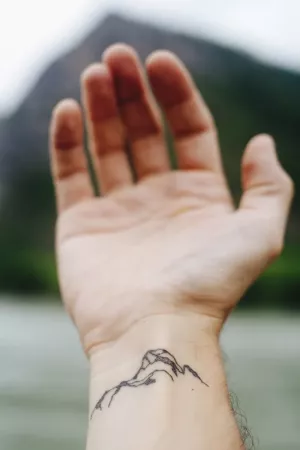 an outstretched hand with a wrist tattoo of a mountain.