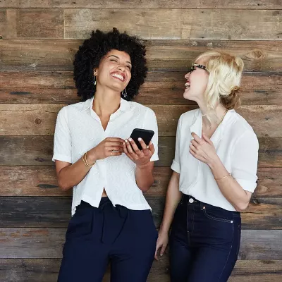 Two women in matching jeans and blouses smiling and laughing.