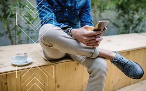 Person sitting on a wooden bench, legs crossed, scrolling on his phone.