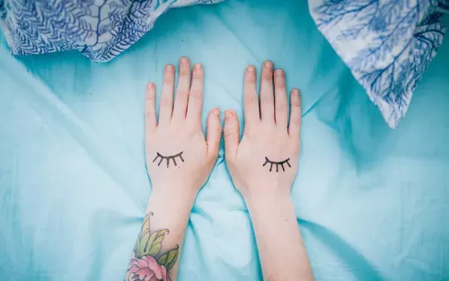 A pair of hands with tattoos rest flat on a blue sheet.