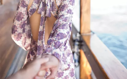 A person holding a woman's hand as she walks forward in a floral dress.