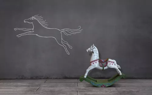 A chalk sketch on a wall of a horse running next to a real rocking horse on the floor.