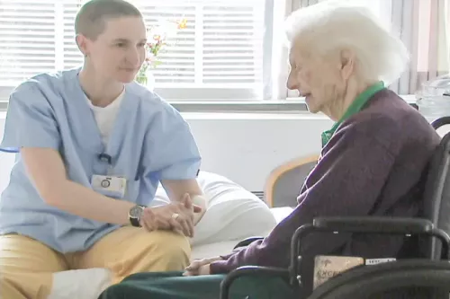 Cal Cates sitting bedside with an elderly client in a wheelchair.