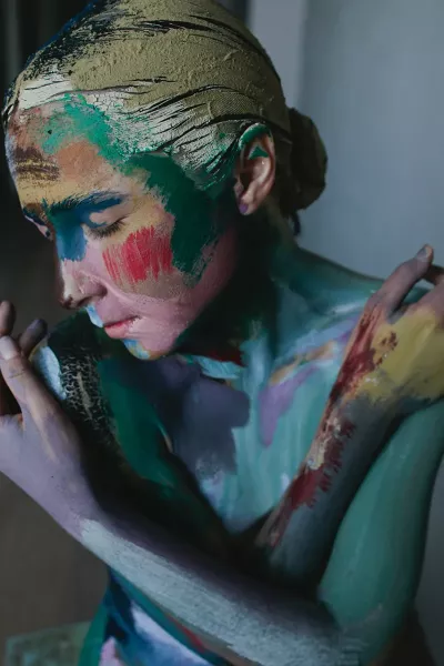 A woman with her whole face, hair, and body covered in streaks of paint.