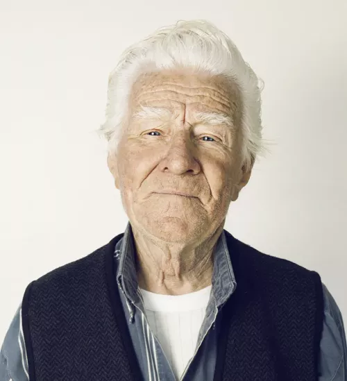 An older man with white hair in an undershirt and collared shirt.