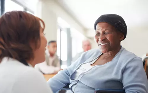 An older Black woman smiles at a massage therapist kneeling near here.