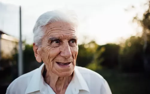 An older man in a collared shirt laughing and smiling.