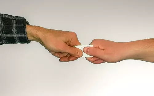 Two people using a thumb and fist to pull on a small piece of paper, demonstrating a test for muscle strength/weakness.