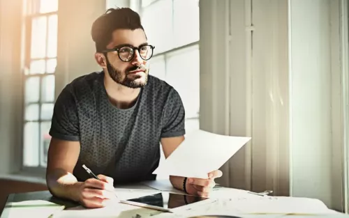 A man at an office desk wearing glasses stares intently off into the distance.