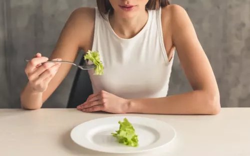 A woman at a table eats a singular piece of lettuce off a plate.