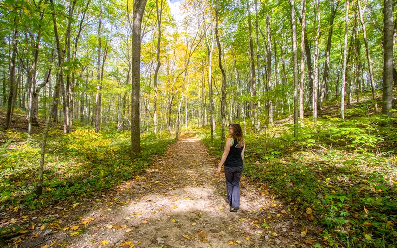 Cindy Williams hikes through a leafy green forest.