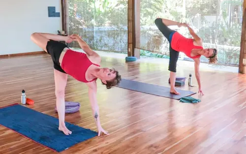 Two women in a room on a natural wooden floor doing yoga.