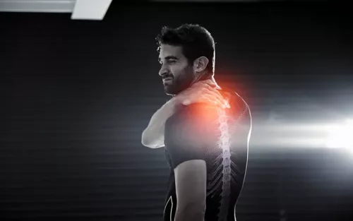 A man holding his upper shoulder and back in pain, redness glows from the affected area.
