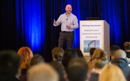 A speaker at the 2018 San Diego Pain Summit shares ideas from the stage, standing in front of a podium.