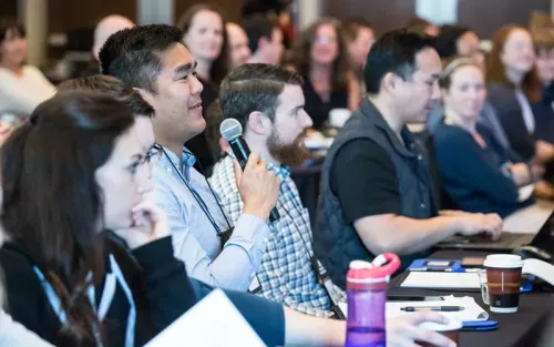 Rows of attendees at the San Diego Pain Summit, with one man holding a mic, sharing their ideas. 