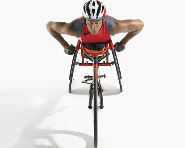 A paracyclist in a red shirt and helmet leans forward in their racing wheelchair.