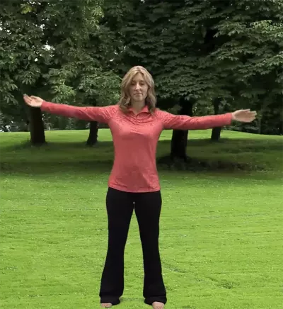 author Angie Parris stands outside on the grass, stretching with her legs and arms outstretched.