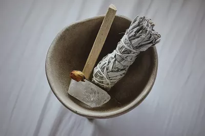 a smudge stick, wood, and a quartz crystal in a bowl.