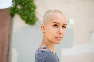 woman with bleached hair and buzzcut looks seriously towards the camera.