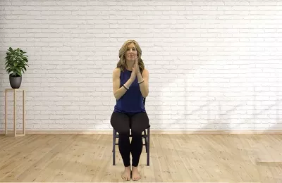 Author Angie Parris holds her hands at heart center while sitting in a chair. 