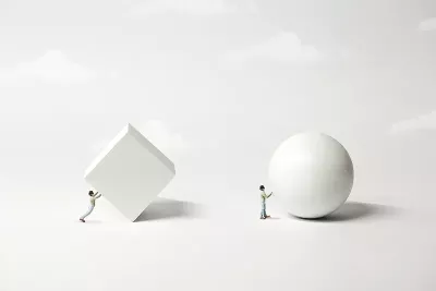 A figure trying to roll a white 3D block, and a second figure rolling a white sphere.