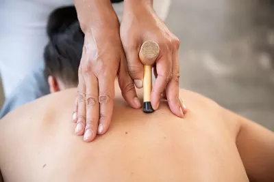 massage therapist uses two hands with a T-bar massage tool on a client's back.