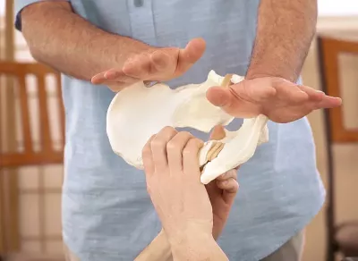male practitioner's hand position on a pelvis bone to demonstrate pressure on a client's ilia for rotation.