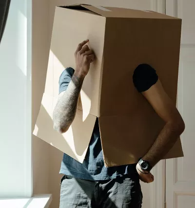 A person wearing a moving box over their head ponders change.