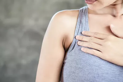 a white woman in a tank top holds a spot on her chest.