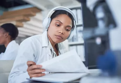 a woman with brown skin tone wearing white headphones reading research.