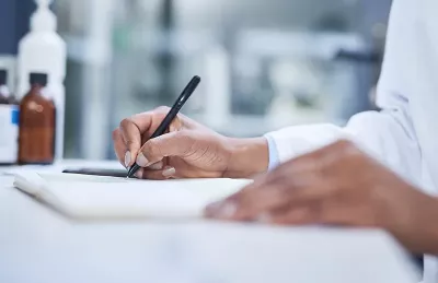 a person's hands use a black pen to write on a sheet of paper.