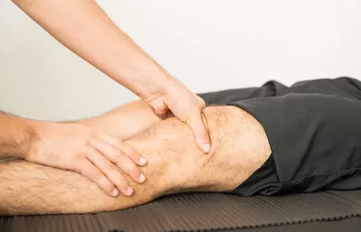 an MT applying pressure around the knee area of a clothed client lying supine.