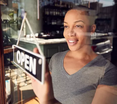 Black woman with short hair changes a business open sign in the window.