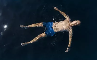 a person in blue swim shorts floats in a dark pool on their back.