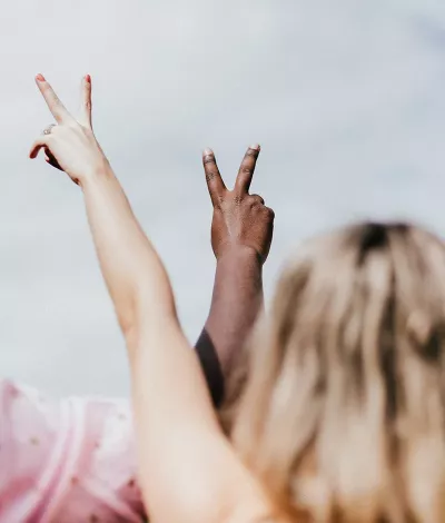 One person with white skin tone and another with dark skin tone make peace signs with their hands.