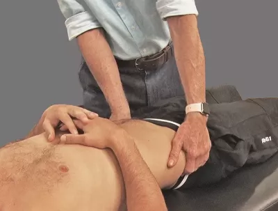 an MT in a collared shirt with sleeves rolled up holding a client's hips to assess for pelvic rotation restrictions.