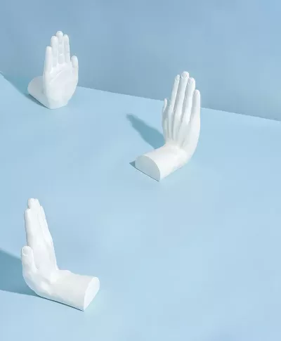 Three porcelain sculptures of hands putting their hands up.