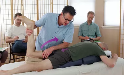 Til Luchau uses a slight downward stabilizing counterpressure on the sacrum of a student during a demonstration. 