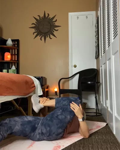 Author Marisa Savino lays flat on her back on the floor, bending one knee towards the chest in pigeon pose.