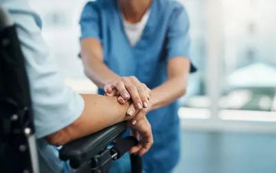 A health professional touches the arm of a client in a wheelchair.