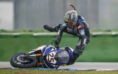 A motorcyle racer falls off his motorcycle as it slides sideways on the ground.