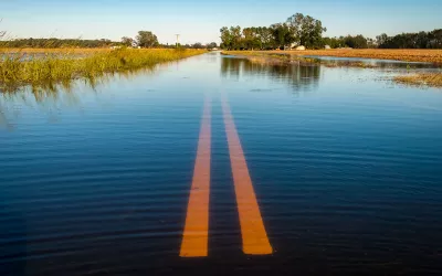 A two-lane road and surrounding fields are flooded with water.