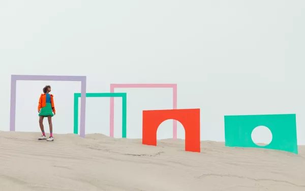 A woman standing on a beach with colorful door frames near her.