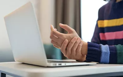 A person working at a laptop rubs their left wrist with their right hand.