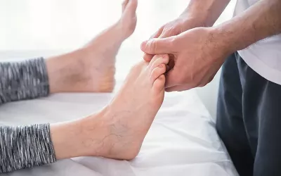 A massage therapist addresses a geriatric client's toes on their right foot.