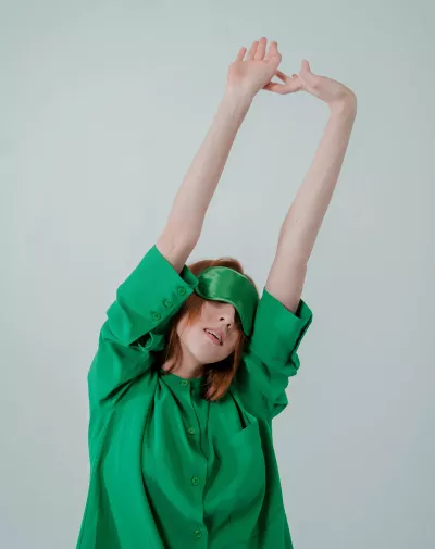 A woman wearing an eye mask stretches her arms upward.
